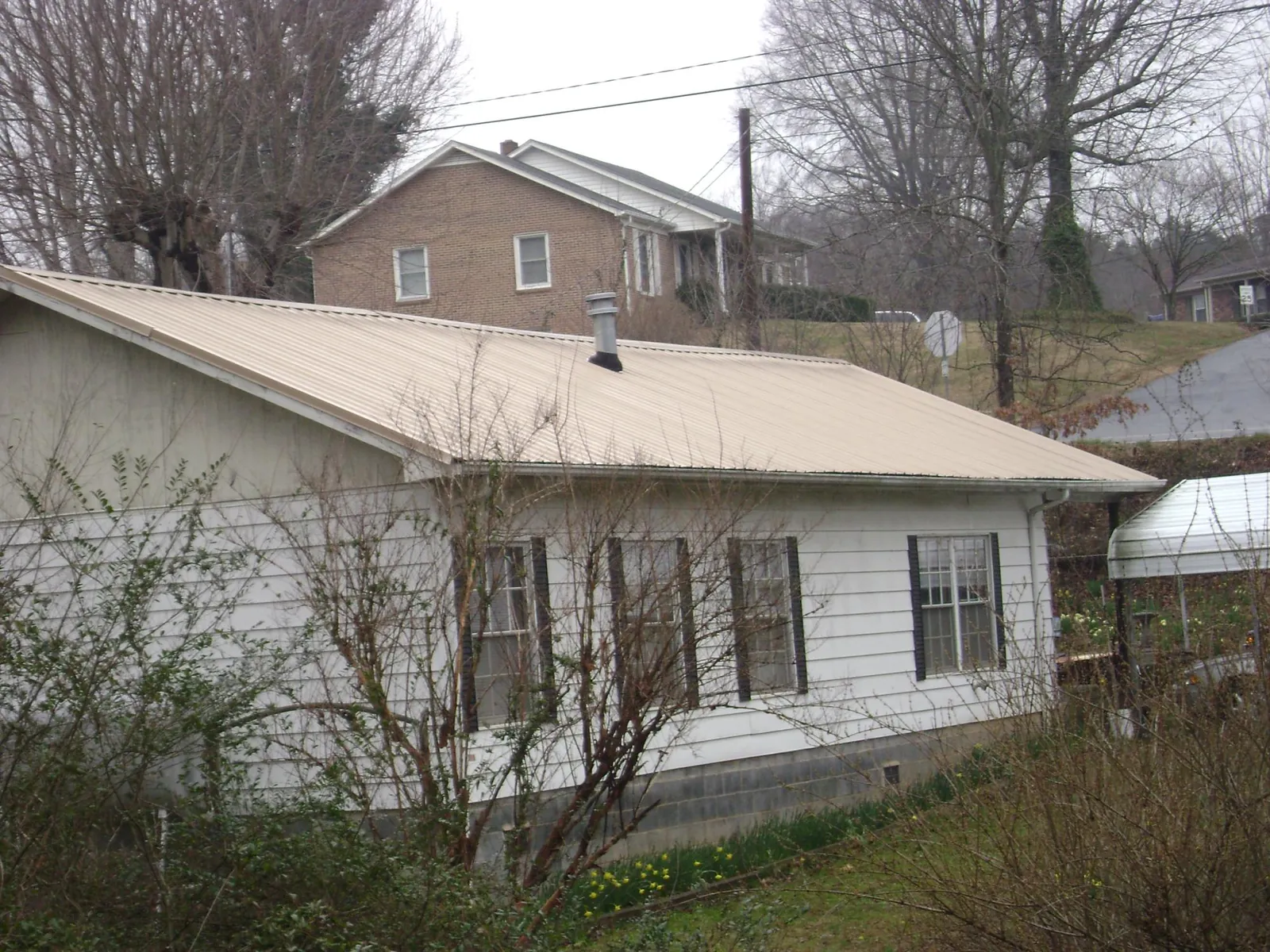 Tan metal roof on a white sided house set into a hillside — Commercial Roofing by Roofing Brothers in Republic